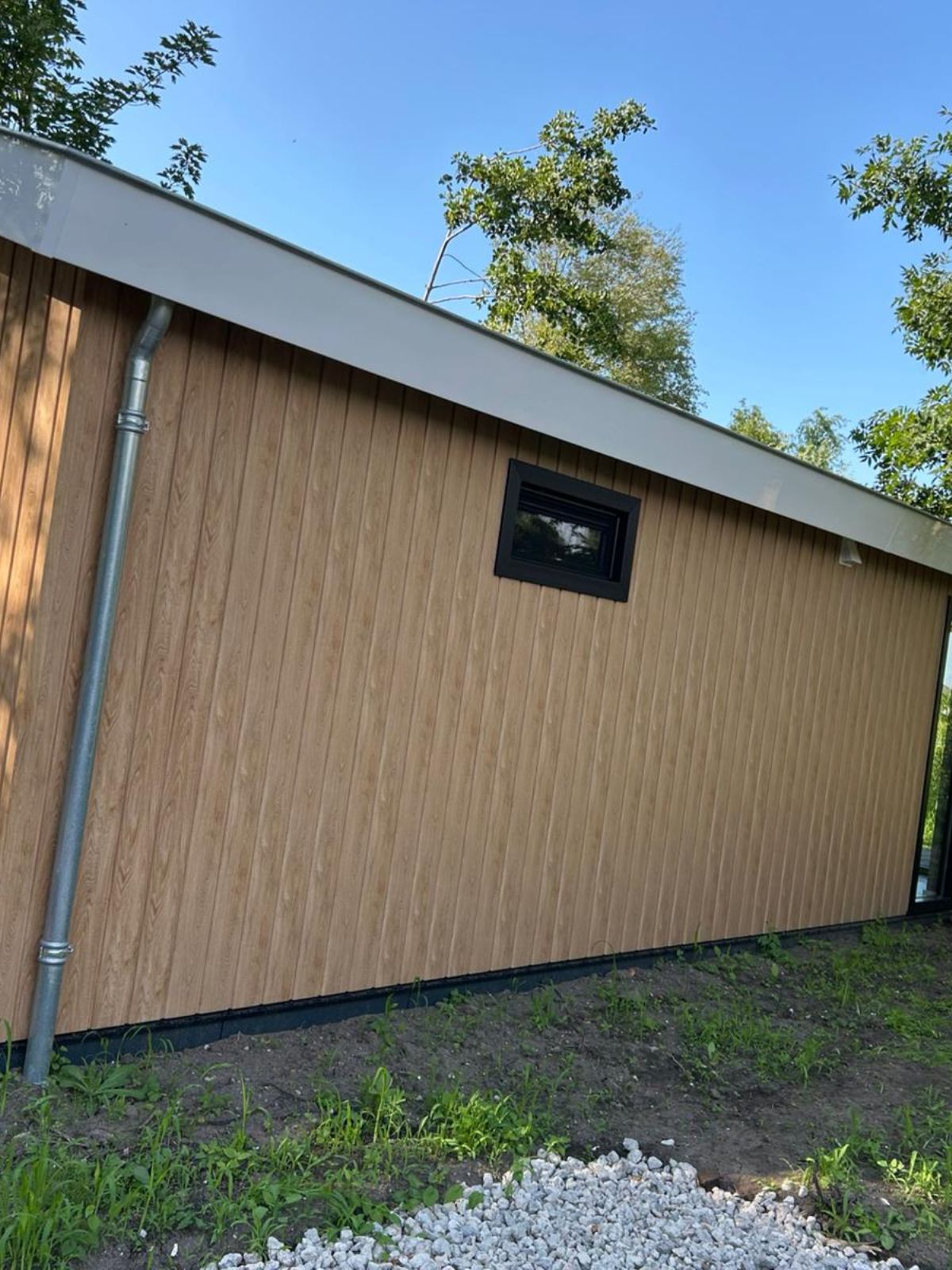 Houten wand van een huis met raam en regenpijp.